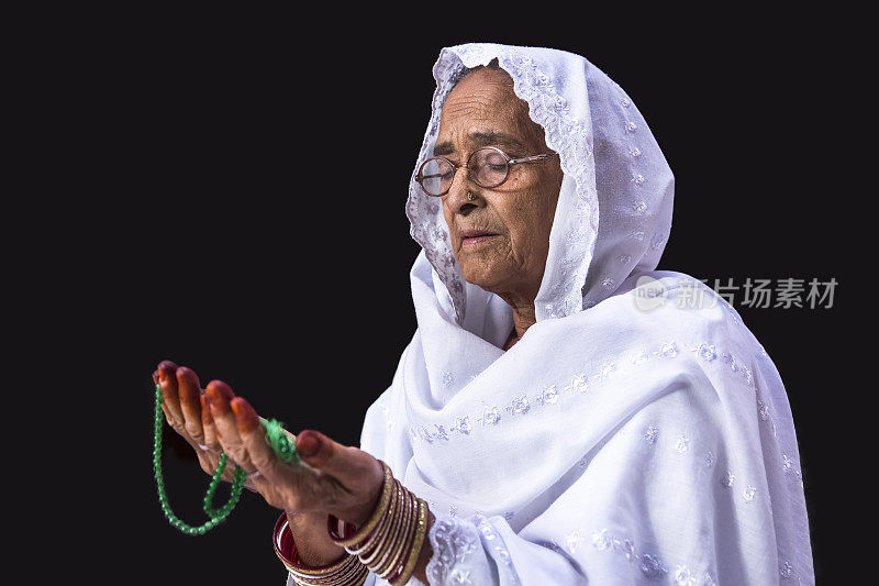 Senior Muslim Woman praying, with prayer beads beads in her hands